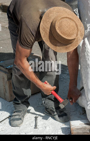 Senior Bildhauer arbeiten im Freien an der Marmorskulptur in seinem Workshop mit Hammer und Meißel Stockfoto