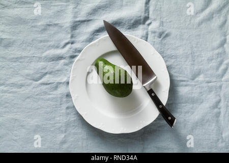 Ganze Avocado- und Kochmesser auf einem Schild an einem Tisch mit einem Blau Leinen Tischdecke Stockfoto