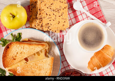 Geröstete Brotscheiben mit Käse, Apfel, Cookies mit ganzen Körnern von Sonnenblumenkernen, Tasse Kaffee und Croissant auf der Untertasse und Glasgefäß mit St Stockfoto