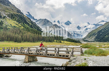 Active Senior, Frau, reiten Ihr e-Mountainbike in das Rosegtal unterhalb der Gletscher und Gipfel der Sella Gruppe und Piz Roseg Stockfoto