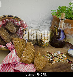 Warenkorb Roggenbrot mit getrockneten rohen Bohnen, Öl auf Holz Oberfläche begleitet. Keramik Topf mit Koriander im Hintergrund. Stock Bild. Stockfoto