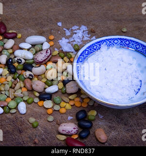 Getrocknete Sortiment trockene bunte Bohnen auf einer hölzernen Oberfläche mit einer Schüssel mit Kristallsalz. Stock Bild. Stockfoto