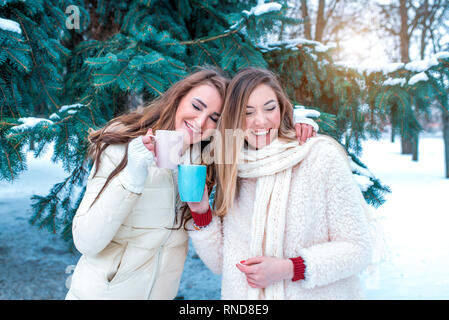 Zwei Mädchen Freundinnen schöne Frauen glücklich Lachen lächelnd. Spaß im Freien im Winter gegen die Kulisse der Weihnachtsbaum. In den Händen der Becher Stockfoto