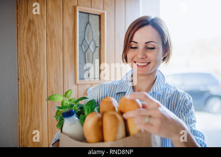 Eine junge Frau, die mit Lebensmitteln in Papier Shopping Bag wandern in durch die vordere Tür. Stockfoto