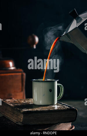 Poring heißen Kaffee in einem Emaille Tasse mit Dampf auf dunklen Stimmung Stockfoto