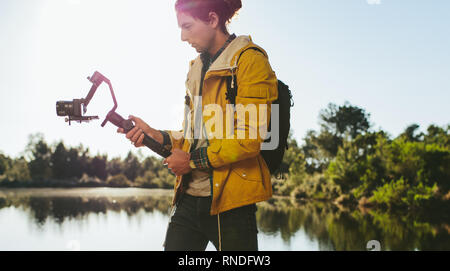 Content Creator schießen ein Video mithilfe einer spiegellosen Kamera auf eine Hand Gimbal montiert. Seitenansicht eines Reisenden an seiner Digitalkamera zu Tak Stockfoto