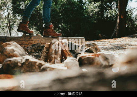 Low Angle View von einer Person zu Fuß auf einem gefallenen Baumstamm in einem Wald. 7/8 Schuß einer Person aus Leder Schuhe Wandern in den Wald. Stockfoto