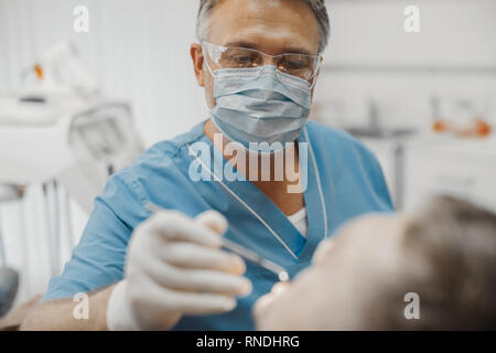 Der Zahnarzt in der blauen Uniform und transparente Gläser Holding zahnmedizinische Instrumente und Überprüfung bis Zähne Gesundheit Zustand. Stockfoto