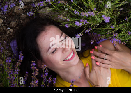 Sommer Portrait von Junge attraktive Frau auf lavendel Feld. Sie trägt einen gelben Kleid, liegend im Inneren blühte der Lavendel und ein Lächeln auf die Lippen kam Stockfoto