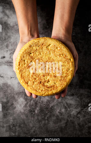 Hohe Betrachtungswinkel von einem kaukasischen Mann mit einer typischen Tortilla de patatas, spanisches Omelette, auf seinen Händen, auf einer grauen Stein Oberfläche Stockfoto
