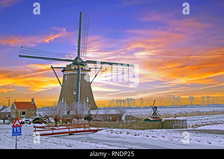 Historische Windmühle in der Landschaft aus den Niederlanden im Winter bei Sonnenuntergang Stockfoto