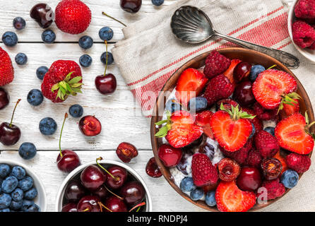 Schüssel von berry Joghurt oder Chia Milchreis mit frischen Himbeeren, Erdbeeren, Kirschen und Heidelbeeren mit einem Löffel. gesundes Frühstück. top View Stockfoto