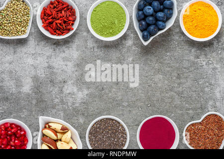 Verschiedene superfoods auf grauem Hintergrund. Superfood, Chia, Matcha, Acai, Kurkuma, Nüsse, Samen, Goji, Blaubeere. Gesunde vegane Ernährung Konzept. Ansicht von oben w Stockfoto