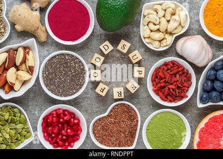 Verschiedene superfoods auf grauem Hintergrund. Matcha, Acai, Kurkuma, Früchte, Beeren, Avocado, Pilze, Nüsse und Samen gesund Vegan essen Top View Stockfoto