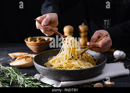 Das traditionelle italienische Nudeln aus der Pfanne. Männliche Hände nehmen Spaghetti in Löffel und Gabel, in low-key-shot Stockfoto