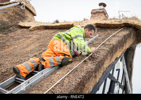 Cambridgeshire, Großbritannien. 18 Feb, 2019. Die strohgedeckten Dach einer alten Ferienhaus Bauernhaus auf Lark Rise Farm wird repariert. Chris Pepper und sein Team arbeiten das denkmalgeschützte Gebäude zu rethatch, Teile aus dem 14. Jahrhundert stammt. Der erfahrene Handwerker mit langem Stroh der Grat wieder aufzubauen und die wichtigsten Teile des Dachs. Credit: Julian Eales/Alamy leben Nachrichten Stockfoto