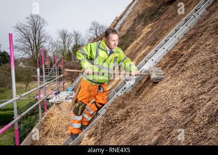 Cambridgeshire, Großbritannien. 18 Feb, 2019. Die strohgedeckten Dach einer alten Ferienhaus Bauernhaus auf Lark Rise Farm wird repariert. Chris Pepper und sein Team arbeiten das denkmalgeschützte Gebäude zu rethatch, Teile aus dem 14. Jahrhundert stammt. Der erfahrene Handwerker mit langem Stroh der Grat wieder aufzubauen und die wichtigsten Teile des Dachs. Credit: Julian Eales/Alamy leben Nachrichten Stockfoto