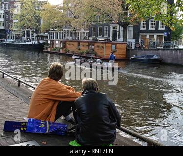 Amsterdam, Niederlande. 9. Okt. 2005. Zwei junge Männer sitzen neben einem Kanal in Amsterdam, Niederlande, mit einem Boot durch. Credit: Arnold Drapkin/ZUMA Draht/Alamy leben Nachrichten Stockfoto