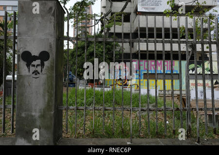 Medellin, Antioquia, Kolumbien. 17 Feb, 2019. Graffiti Schablone auf Bauzaun des Monaco mit escobar Gesicht und Micky Maus Ohren und einem bunten Graffiti auf die Fassade des Gebäudes mit dem Wort 'Umwandeln'' 25 Jahre nach dem Tod von Pablo Escobar, der MedellÃ n Mayor's Office und die Gemeinschaft die Monaco Gebäude abzureißen und eine Gedenkstätte für die Opfer der Escobar Krieg errichten. Das Gebäude wurde als ein Luxus Bunker vom Capo, selbst zu halten und seine Familie sicher gebaut, und als die MedellÃ-n-Kartell Sitz.. Der Monaco Gebäude ein Problem für t Stockfoto