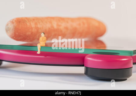 Miniatur Frau Abbildung verlegen auf die digitale elektronische Personenwaage, die für das Gewicht des menschlichen Körpers. Frisches Gemüse bei geringer Tiefenschärfe Hintergrund Stockfoto