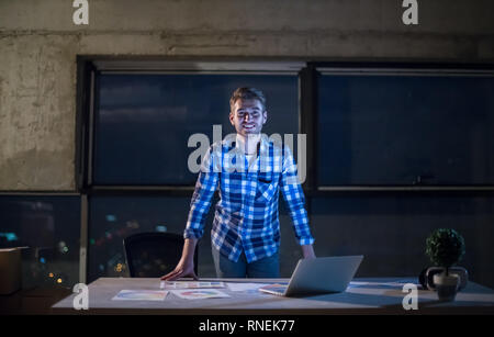 Portrait von jungen männlichen Ingenieur auf Baustelle Prüfung von Dokumenten und Business Workflow mit Laptop Computer in neue Start Büro bei Nacht Stockfoto