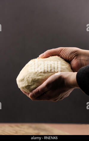 Jemand eine Pizza Teig mit beiden Händen auf einem dunklen Hintergrund Stockfoto