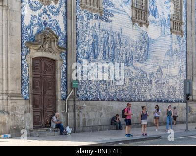 Ein armer Mann sitzt in der schweren verzierten, Türöffnung, die eine blaue Schale außerhalb Carmo Kirche Wand der blauen Keramikfliesen in Porto, Portugal Stockfoto