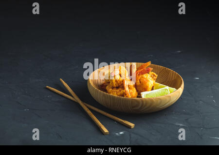 Gebratene Garnelen tempura mit Kalk in Holzplatte auf dunklen Betonoberfläche Hintergrund. Kopieren Sie Text. Tempura Meeresfrüchte Teller serviert japanische oder Stockfoto