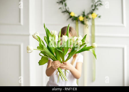 Portrait einer hübschen kleinen Mädchen in einem weißen Hemd versteckt sich hinter einem Bouquet von weißen Tulpen Stockfoto