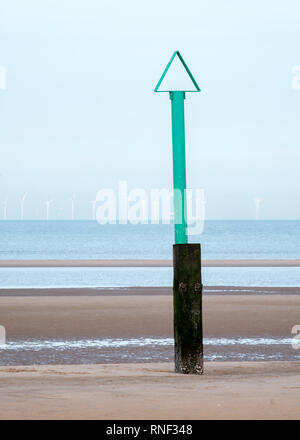 Ein Green Beach safety Marker mit einem Dreieck auf der Oberseite und eine Offshore Windparks in der Entfernung aus Rhyl Beach, Denbighshire, North Wales Stockfoto