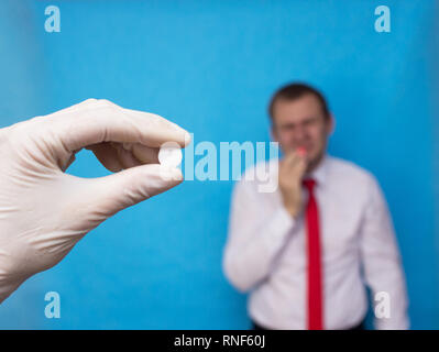 Der Arzt hält eine Pille in die Hand für orale Herpes, ein Mann, der zu ihr Lippe, Herpes hält, Pillen gegen Herpes, Infektion Stockfoto