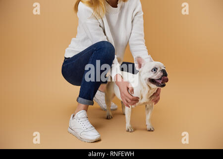 7/8-Ansicht der Frau in weißen Pullover mit Französische Bulldogge auf beigen Hintergrund Stockfoto