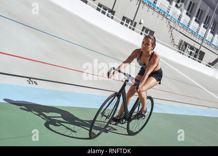 In voller Länge Porträt der jungen Athleten in schwarz Sportbekleidung mit dem Fahrrad auf der Rennstrecke. Sie ist auf Reiten konzentriert Stockfoto