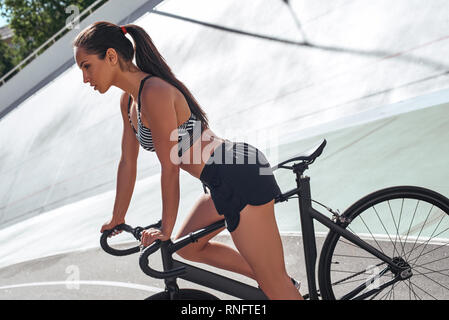 Porträt der jungen Athleten in schwarz Sportbekleidung mit dem Fahrrad auf der Rennstrecke. Sie ist auf Reiten konzentriert. Seitenansicht Stockfoto