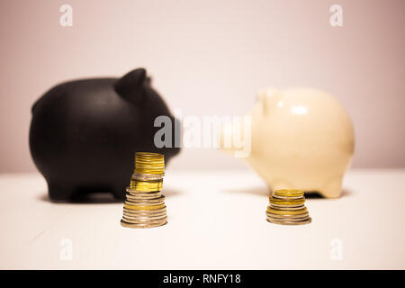 Schwarze und weiße piggy Bank Sparschwein mit Münzen neben Ihnen als Aufwendungen und Einsparungen gestapelt. Stockfoto