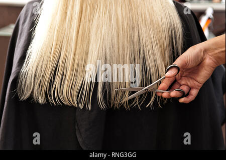 Feuchte lange, blonde Haare auf schwarzem Grund mit Hand sterben eine Schere haelt. [(C) Dirk Friedrich A. Stockfoto