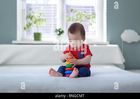 Baby Boy mit farbigen Pyramide Spielzeug auf Bett in seinem Zimmer Stockfoto