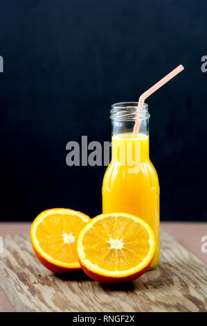 Noch immer leben von Orangensaft in einer kleinen Flasche und eine Orange in zwei Lager gespalten, die sich alle auf eine alte Holz- und dunklen Hintergrund Stockfoto