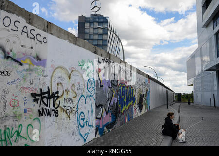 Deutschland, Berlin, die Mauer, East Side Gallery, Wand paintíngs und Wandmalereien über den Kalten Krieg und die Wände, Graffitis auf der Rückseite, hinter Gebäude mit Mercedes Benz Stern, das Symbol der West deutscher Automobilhersteller Stockfoto