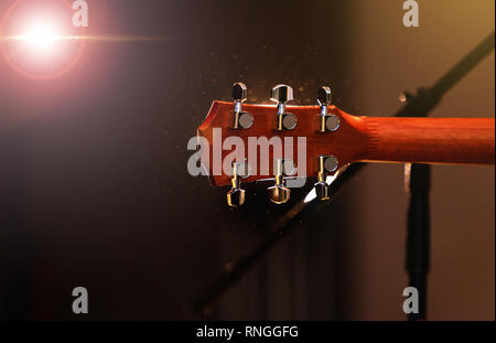 Akustik Gitarre Kopf mit Stimmwirbel, Hals, Bünde und Griffbrett, Ansicht von hinten. Kopfplatte der Gitarre über konzertbühne Hintergrund mit Licht flare Stockfoto