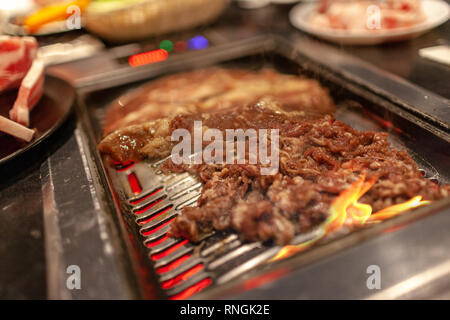 Koreanisches Barbecue mit saftigen Rindfleisch und Rippchen am heißen Herd Platte mit Feuer und Rauch emitting vom Kochen. Stockfoto