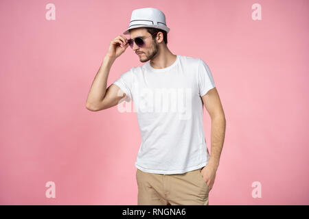 Fröhlicher junger Mann mit Hut und Sonnenbrille und lächelnd über rosa Hintergrund. Stockfoto