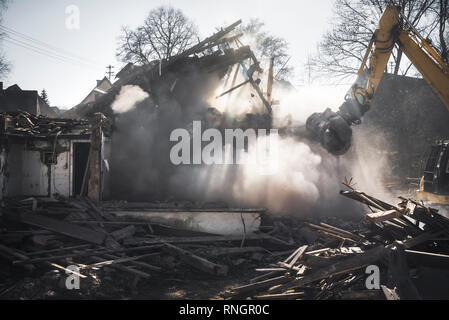 Abriss eines alten Deutschen Haus mit einem Bagger. Haus stürzt in eine Staubwolke und Sonnenstrahlen. Baustelle. Stockfoto