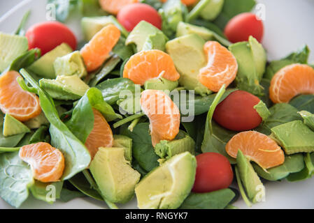 Nahaufnahme von rohem Obst und Gemüse Salat mit Spinat, Mandarinen, Trauben Tomaten und Spinat auf eine weiße Platte. Stockfoto