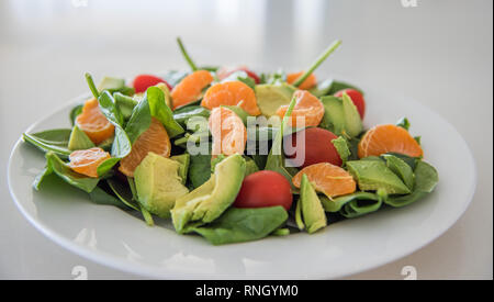 Nahaufnahme von rohem Obst und Gemüse Salat mit Spinat, Mandarinen, Trauben Tomaten und Spinat auf eine weiße Platte. Stockfoto