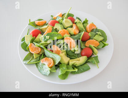 Nahaufnahme von rohem Obst und Gemüse Salat mit Spinat, Mandarinen, Trauben Tomaten und Spinat auf eine weiße Platte. Stockfoto