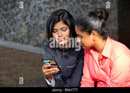 Zwei junge indische Mädchen saßen und auf ihr Mobiltelefon, Pune Stockfoto