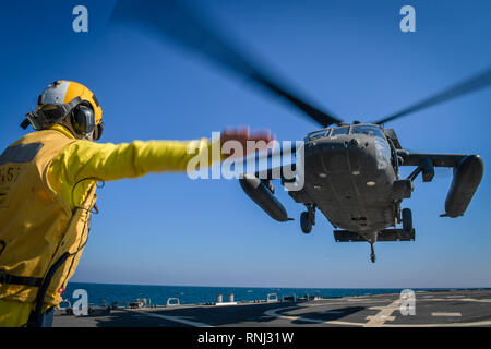 190204-N-OW 182-4229 arabischen Golf (Feb. 4, 2019) Bootsmann Mate 1. Klasse Daniel Linsalata Signale Befehle an ein UH-60 Black Hawk Hubschrauber, zu Task Force Javelin zugeordnet, auf dem Flugdeck der Arleigh-Burke-Klasse geführte Anti-raketen-Zerstörer USS Mitscher (DDG57). Mitscher ist in die USA 5 Flotte Bereich der Maßnahmen zur Unterstützung der Marine im Einsatz für die Stabilität und Sicherheit in der Region zu gewährleisten und verbindet das Mittelmeer und den Pazifischen Raum durch den westlichen Indischen Ozean und drei strategischen Punkten ersticken. (U.S. Marine Foto von Mass Communication Specialist 2. Klasse J Stockfoto