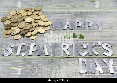 Inschrift happy Patricks Tag, eine Menge Gold britische Münzen und drei Blätter mit Klee, liegen auf einer strukturierten Holzbrett Stockfoto