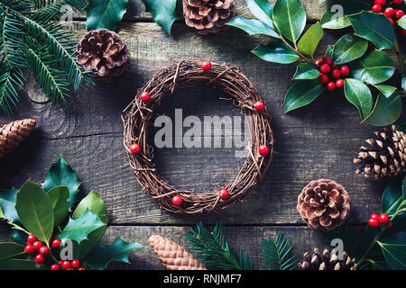 Machen Weihnachten Kranz mit frischen und natürlichen Materialien. Weihnachten Kranz mit roten Beeren und Kegel auf Holztisch. Stockfoto